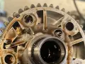 Metalowe koło zmiennych faz rozrządu, pokryte olejem, z widocznymi elementami mechanicznymi i zębatkami.