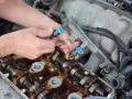 Mechanik wymienia wtryski paliwa, dbając o czyszczenie układu paliwowego. Widać jego dłonie przy silniku.