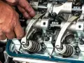 Mechanik reguluje zawory w silniku. Widać precyzyjne części i wałki z napisem "REID".