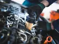 Mechanik w czarnych rękawiczkach wymienia filtr paliwa w silniku samochodu.