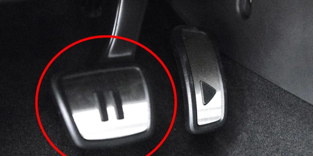 Metalowe pedały w samochodzie, jeden z symbolem "II" (auto hold) i drugi z trójkątem.