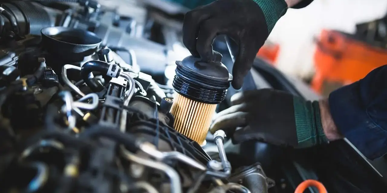 Mechanik w czarnych rękawiczkach wymienia filtr paliwa w silniku samochodu.