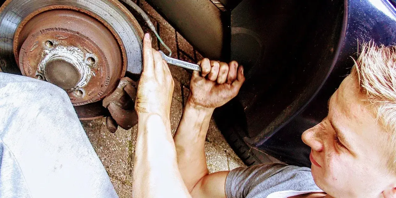 Mechanik z kluczem przy kole samochodu, wymiana łożyska.