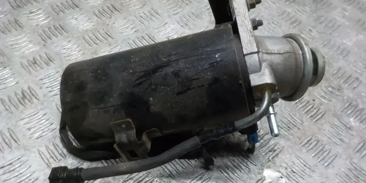 Filtr paliwa z widocznymi przewodami i mocowaniem na metalowym tle.