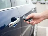 Dłoń trzyma kluczyk keyless, zbliżając go do klamki ciemnoniebieskiego samochodu.