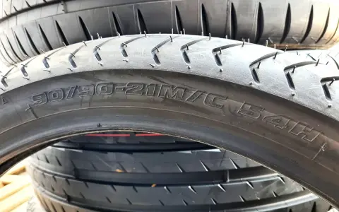 Opona motocyklowa z oznaczeniem 90/90-21M/C 54H. Szerokość opony jest kluczowa dla przyczepności.