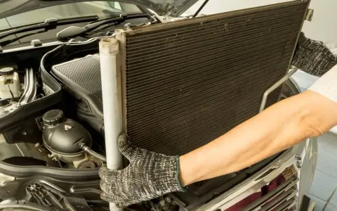 Mechanik w rękawicach wyjmuje chłodnicę klimatyzacji z silnika samochodu.