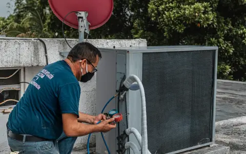 Technik sprawdza czujnik ciśnienia klimatyzacji, podłączając manometr do jednostki zewnętrznej.