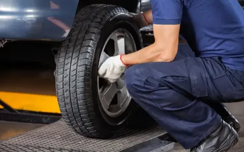 Mechanik w białych rękawiczkach dokręca śruby koła. Czas pomyśleć, kiedy wymienić opony na letnie.
