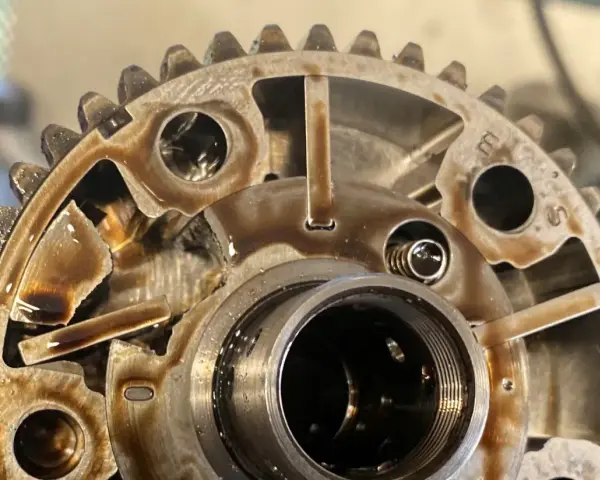 Metalowe koło zmiennych faz rozrządu, pokryte olejem, z widocznymi elementami mechanicznymi i zębatkami.