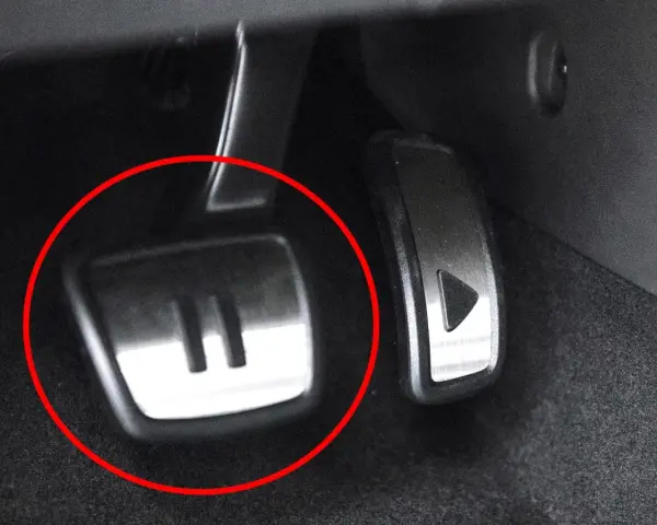 Metalowe pedały w samochodzie, jeden z symbolem "II" (auto hold) i drugi z trójkątem.