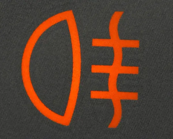 Pomarańczowy symbol świateł mijania na ciemnoszarym tle. Ikona przedstawia reflektor z trzema poziomymi liniami.