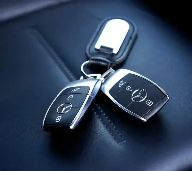 Dwa kluczyki samochodowe Mercedes-Benz z immobilizerem, leżące na skórzanym siedzeniu.