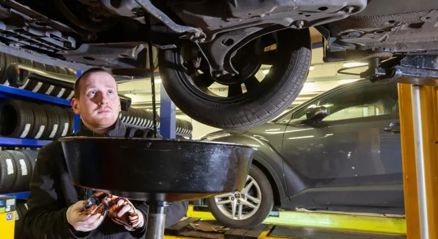 Mechanik wymienia olej w samochodzie, trzymając miskę z zużytym płynem.