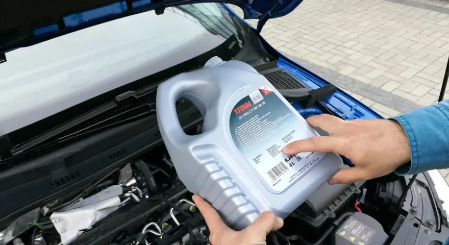 Osoba trzymająca kanister oleju silnikowego TITAN GT1 PRO C-3 SAE 5W-30 nad silnikiem. Czy można mieszać oleje silnikowe? Sprawdź specyfikacje!