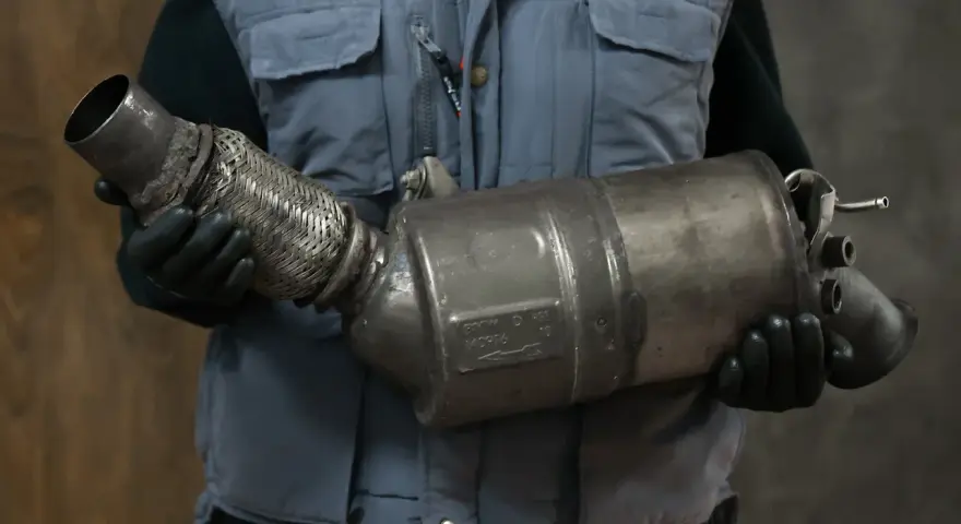 Mechanik w rękawiczkach trzyma zużyty element układu wydechowego, prawdopodobnie po problemach z wypalaniem DPF.
