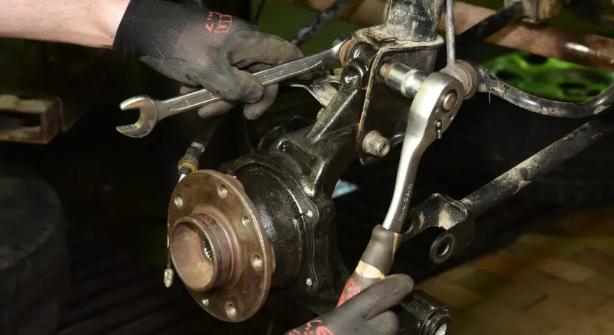 Mechanik w rękawiczkach używa kluczy do wymiany łożyska w samochodzie.