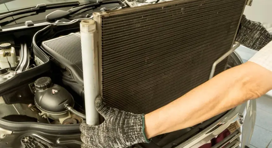 Mechanik w rękawicach wyjmuje chłodnicę klimatyzacji z silnika samochodu.