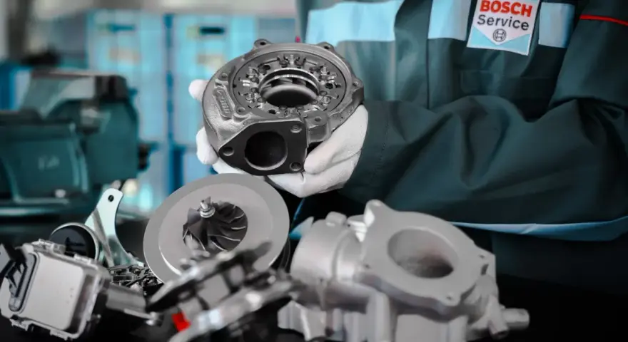 Mechanik w białych rękawiczkach prezentuje części turbiny. Na stole leżą wirnik i obudowa, gotowe do montażu.