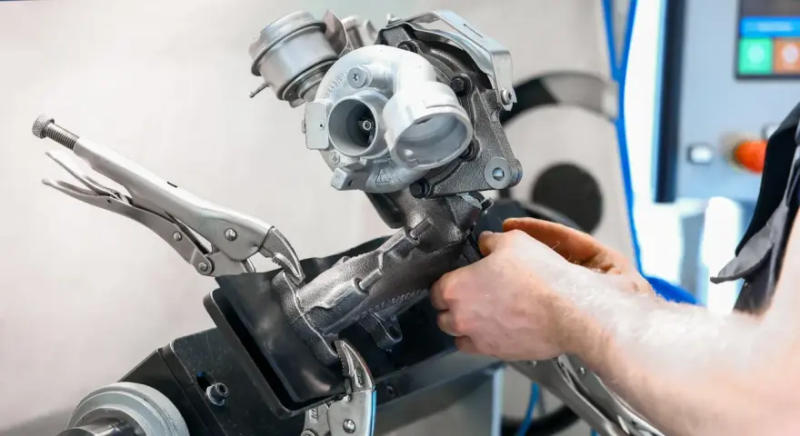 Mechanik pracuje nad turbosprężarką, mocując ją imadłem. Widoczny jest zawór N75, kluczowy element sterujący pracą turbiny.