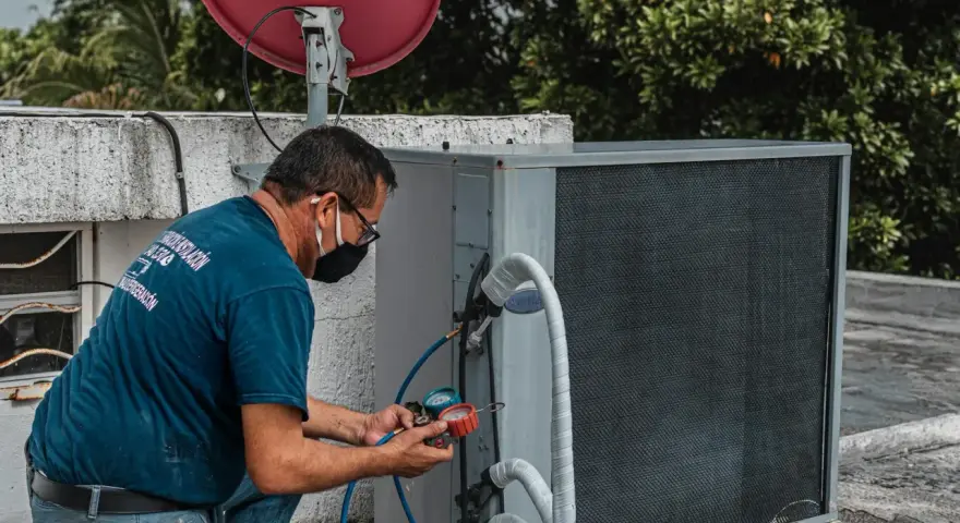 Technik sprawdza czujnik ciśnienia klimatyzacji, podłączając manometr do jednostki zewnętrznej.