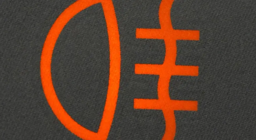Pomarańczowy symbol świateł mijania na ciemnoszarym tle. Ikona przedstawia reflektor z trzema poziomymi liniami.