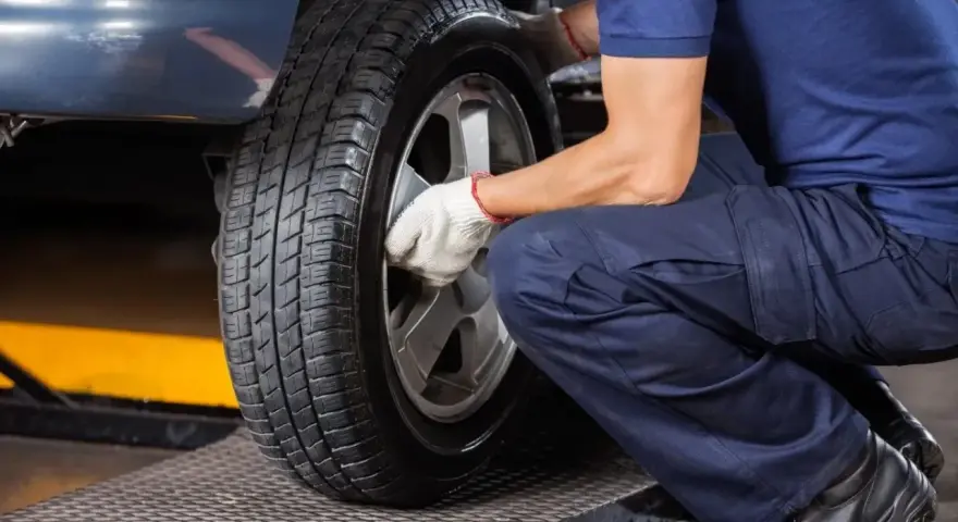 Mechanik w białych rękawiczkach dokręca śruby koła. Czas pomyśleć, kiedy wymienić opony na letnie.