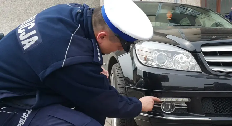 Policjant sprawdza, jakie światła do jazdy dziennej zamontowano w czarnym Mercedesie.