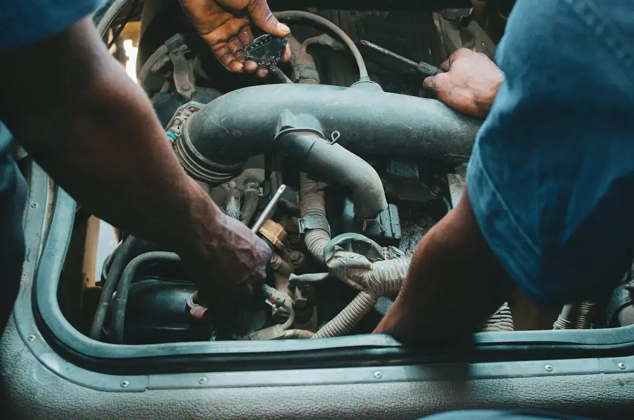 Mechanicy pracują przy silniku, jeden z nich trzyma wtyczkę, drugi dokręca śrubę. Może to być zawór par paliwa.