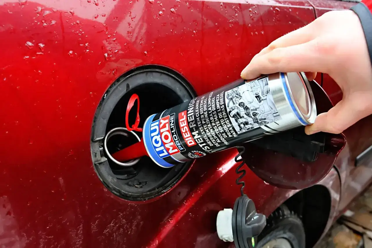 Dłoń wlewa preparat do czyszczenia wtrysków diesel do baku czerwonego samochodu.