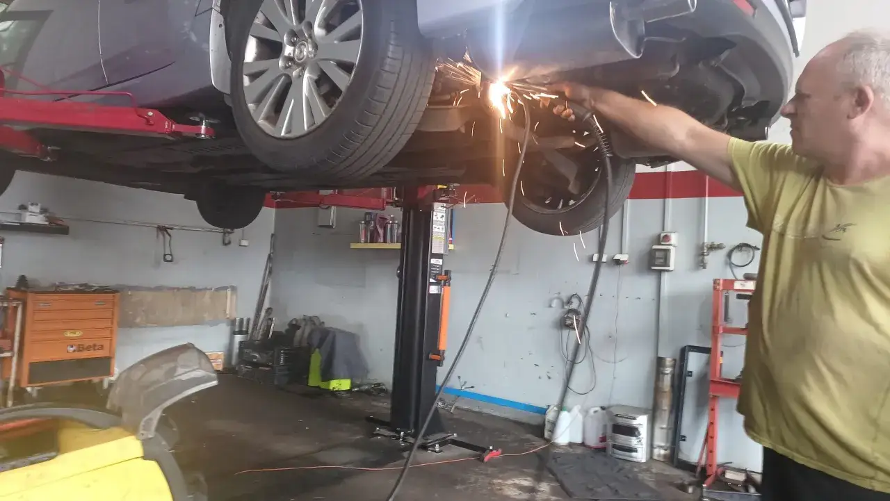 Mechanik spawa dziurę w tłumiku samochodu na podnośniku.