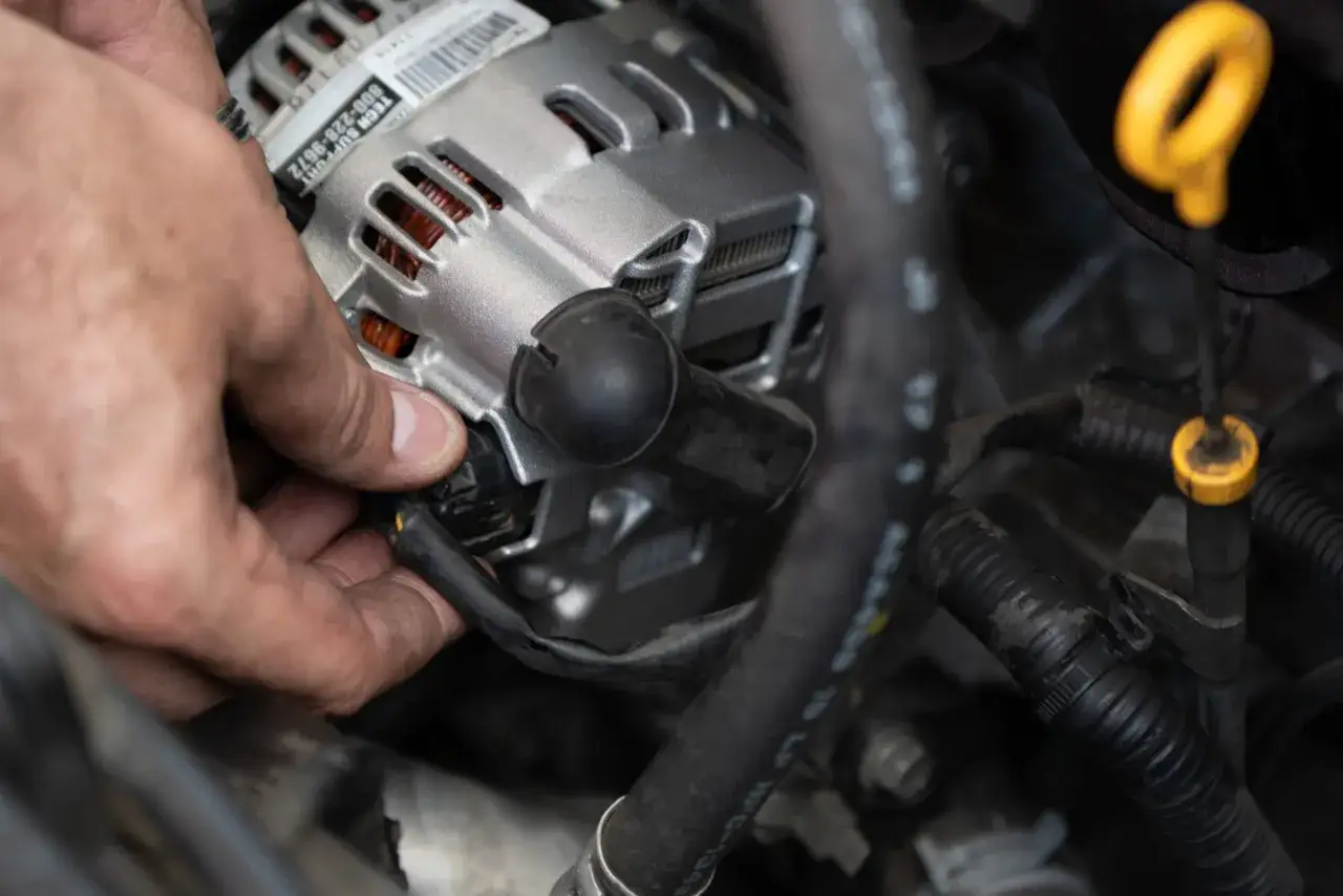 Dłoń mechanika podłącza wtyczkę do stojan alternatora w samochodzie.
