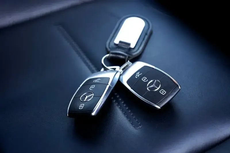 Dwa kluczyki samochodowe Mercedes-Benz z immobilizerem, leżące na skórzanym siedzeniu.